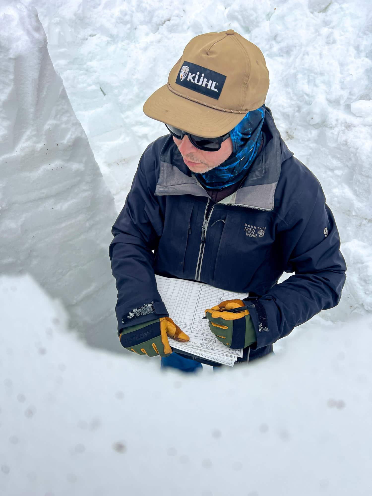 Вид сверху на исследователя, стоящего в снежной траншее с планшетом с записями