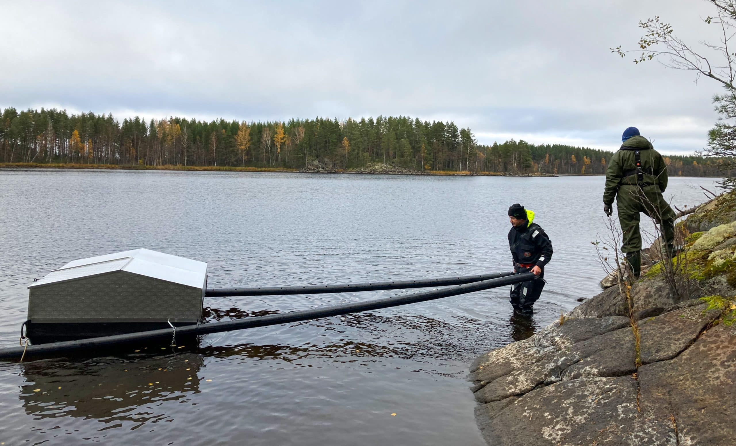 Два человека держат трос, прикрепленный к плавучей конструкции на озере