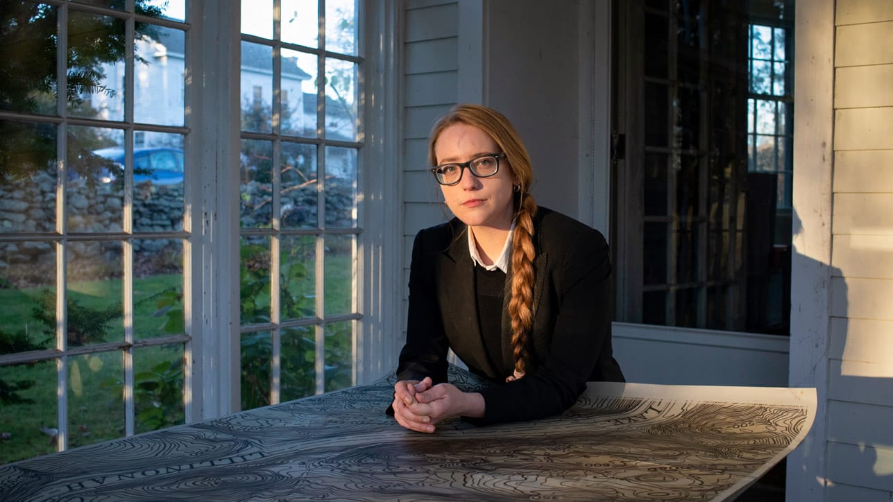 Молли Бурханс опирается на столешницу, на которой разложена большая карта