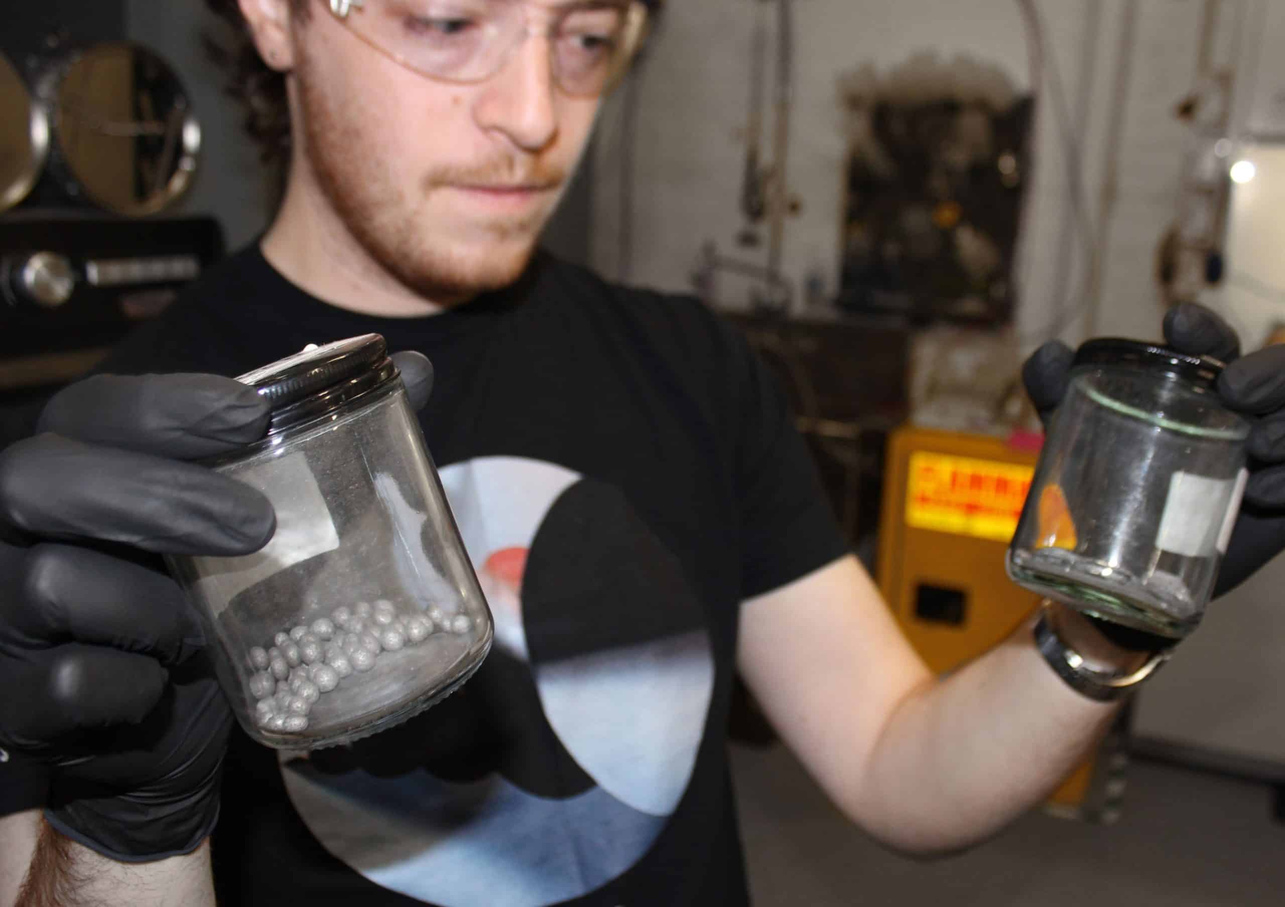 Петр Годарт держит две стеклянные банки; одна с металлическими сферами, другая с плоскими металлическими фигурами