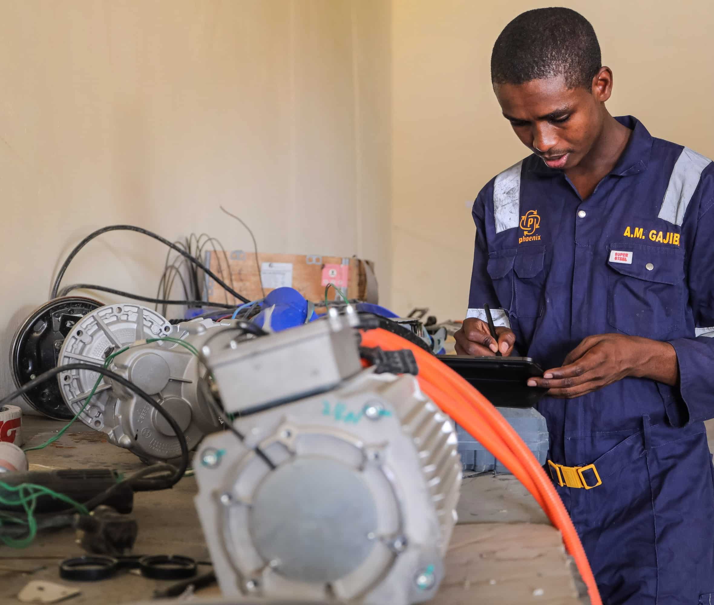 Мустафа Гаджибо за верстаком с деталями мотора на переднем плане